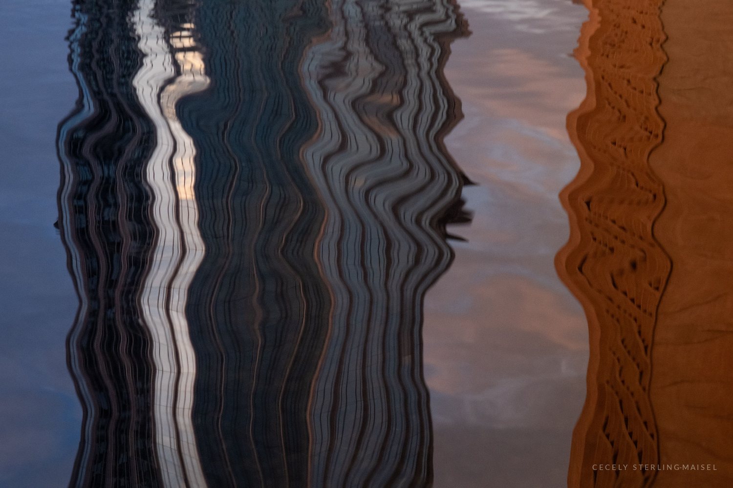 Close-up of water reflecting a glass tower and a warm brick facade, the vertical lines stretched into wavy ribbons.