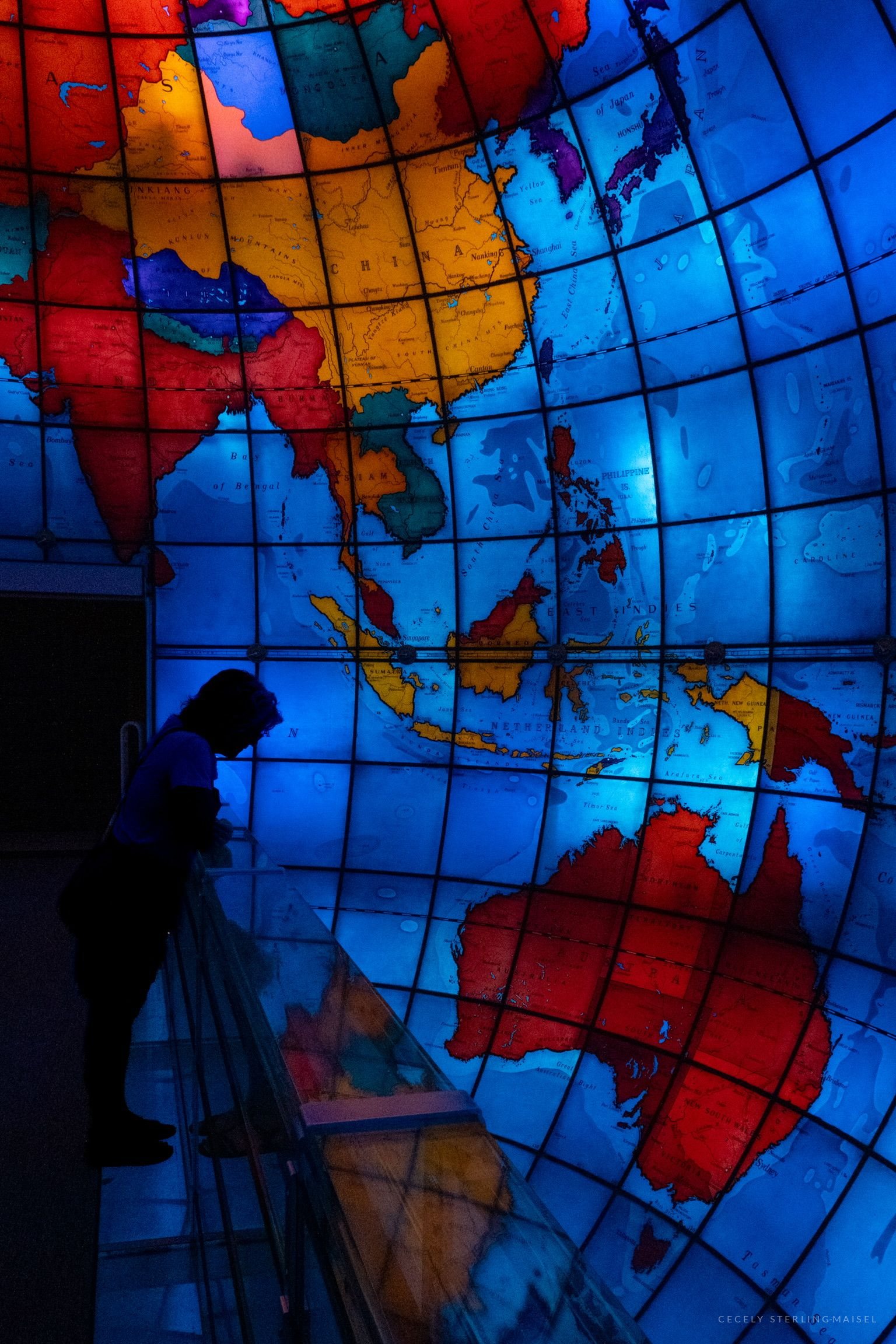 A silhouetted figure before a vast illuminated stained-glass globe, continents glowing red and blue.