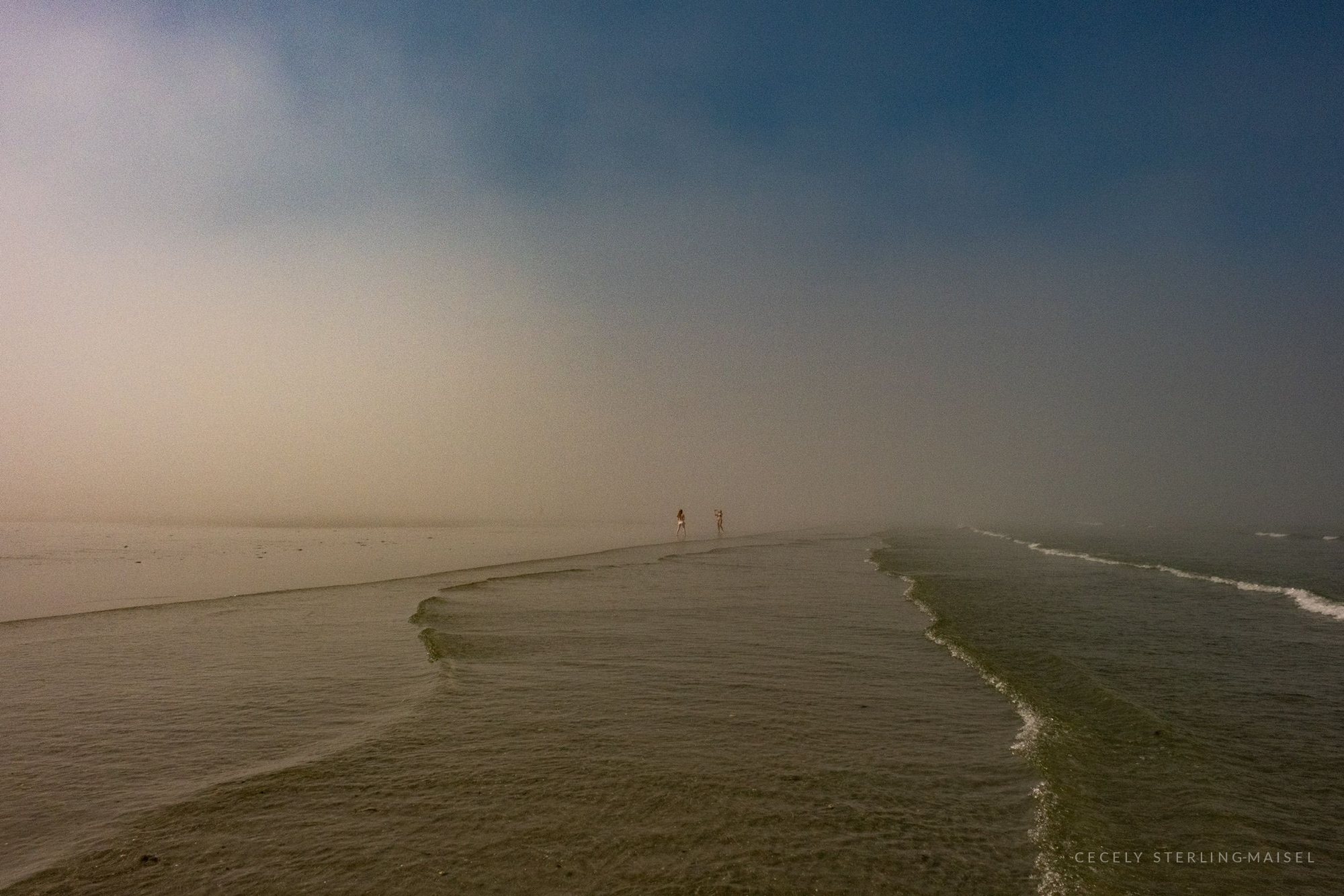 A long breakwater curving out into dense fog until the horizon disappears entirely.