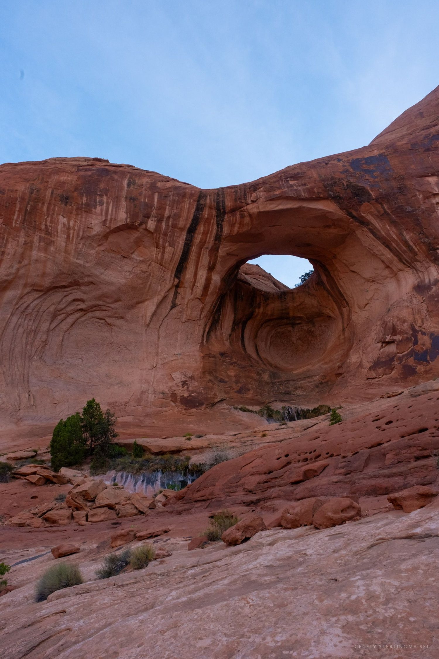 A rounded arch high on a sandstone wall, its opening a dark eye against blue sky.