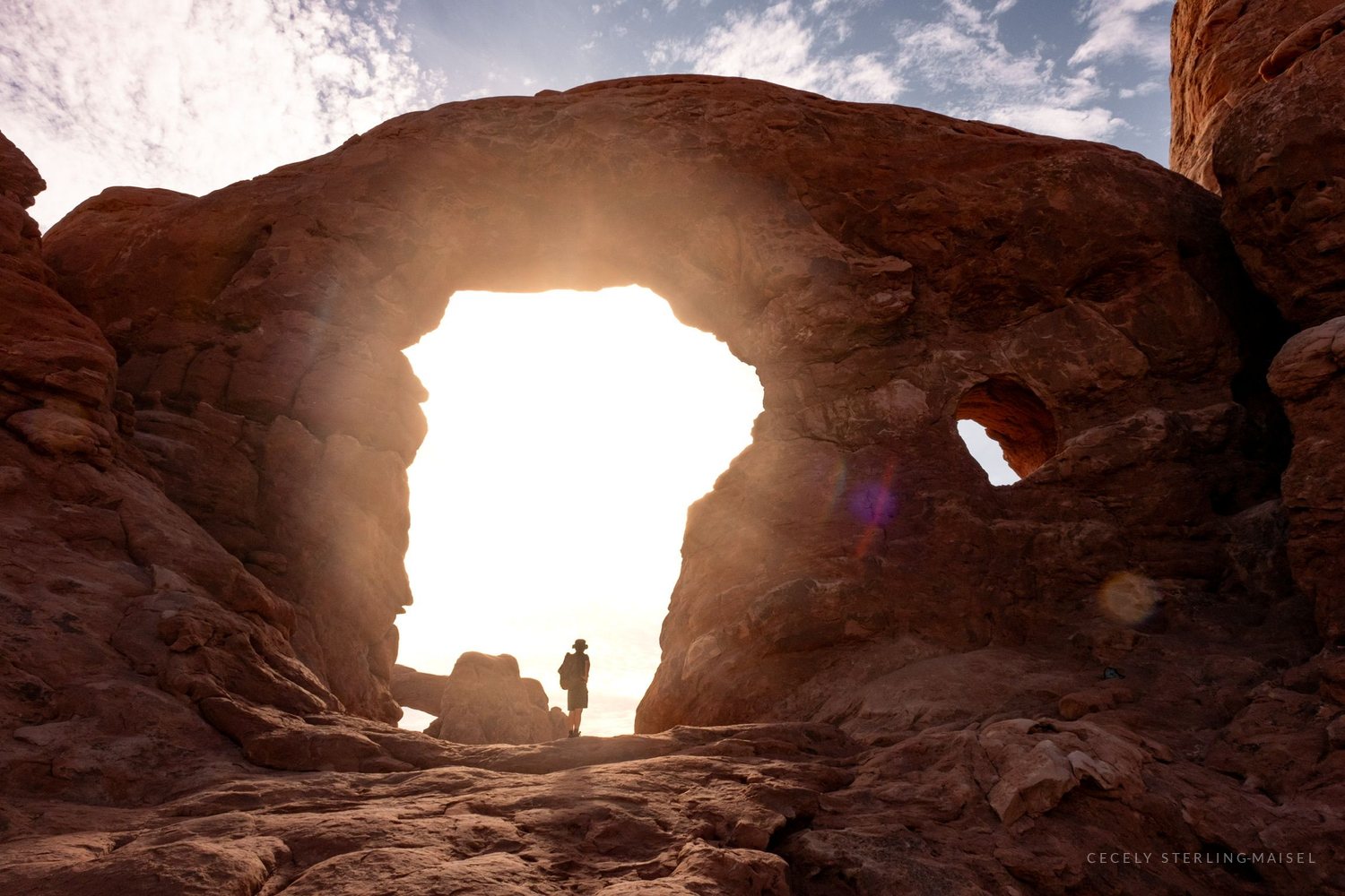 A figure standing in the opening of Turret Arch with the sun blazing through behind them.