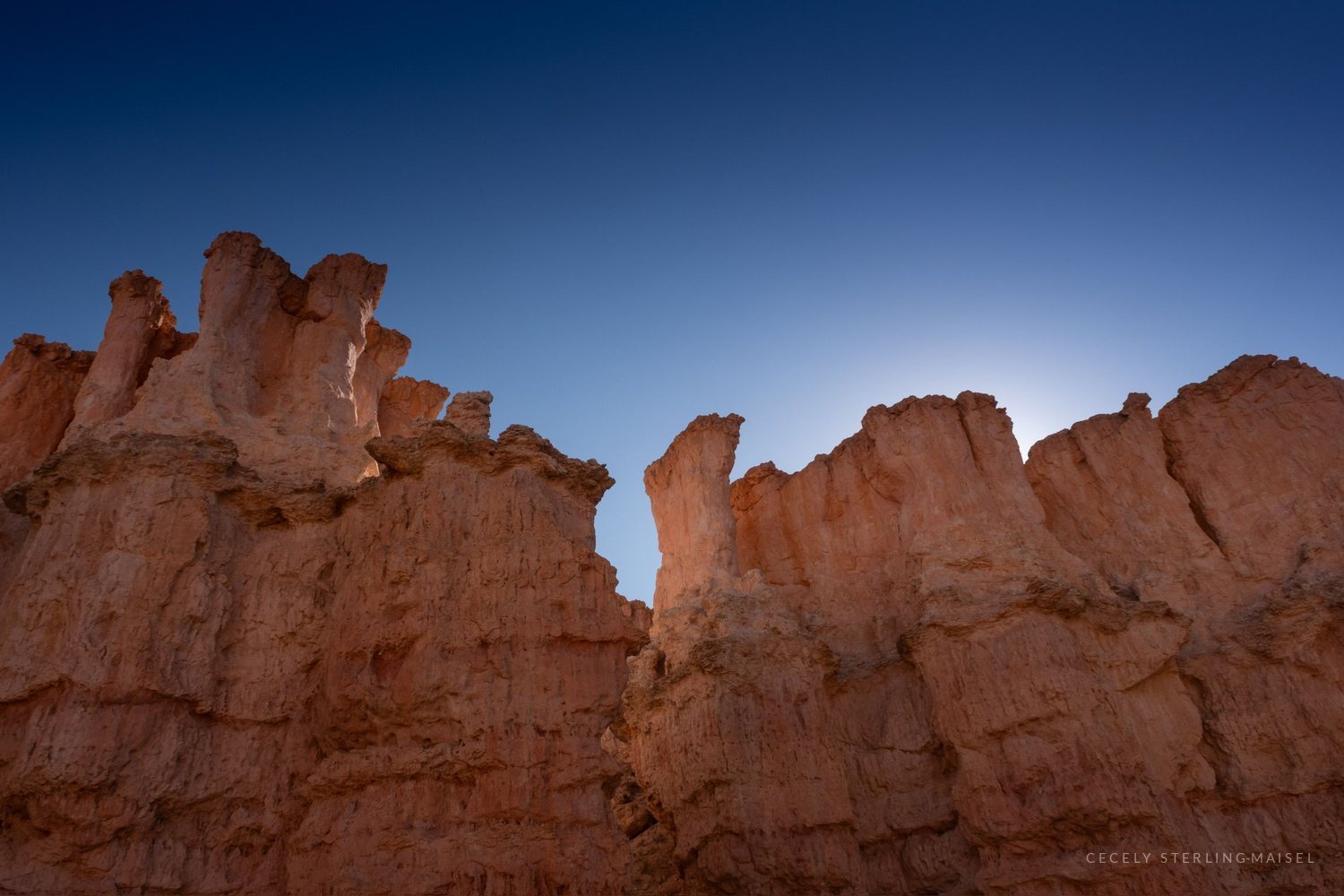 Hoodoos lit from behind at sunrise, the sun rising in a gap between two spires.