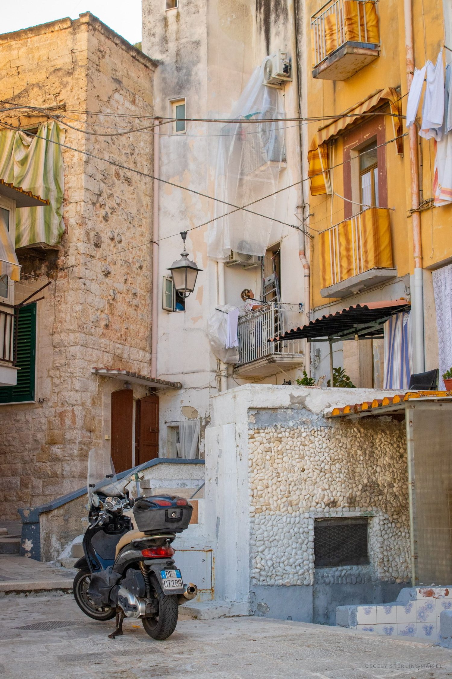 A narrow southern Italian alley with yellow shutters, hanging laundry and a parked scooter.